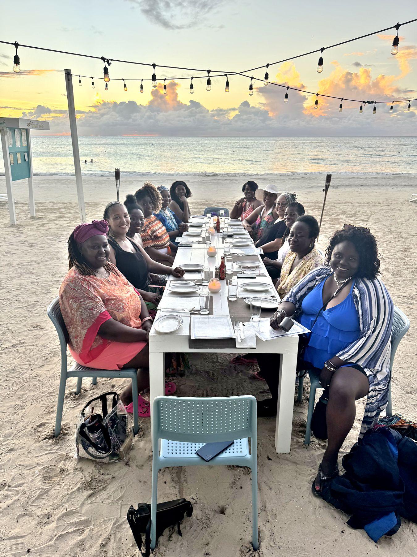 Women gathered at a long candlelit table on the beach at sunset in Negril