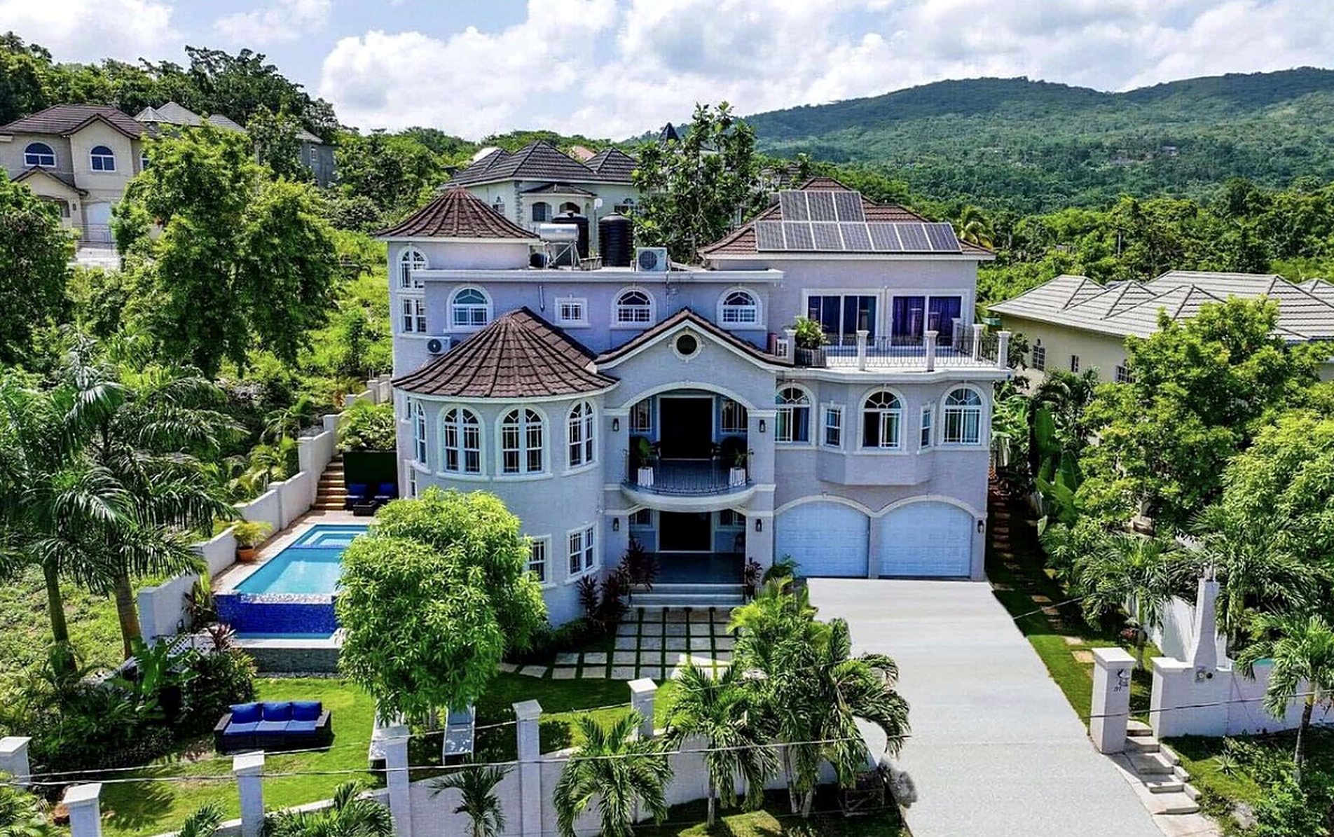 Aerial view of M.O.S.A.I.C. Luxury Villa, a white hillside home with a pool, palms, and green mountains behind