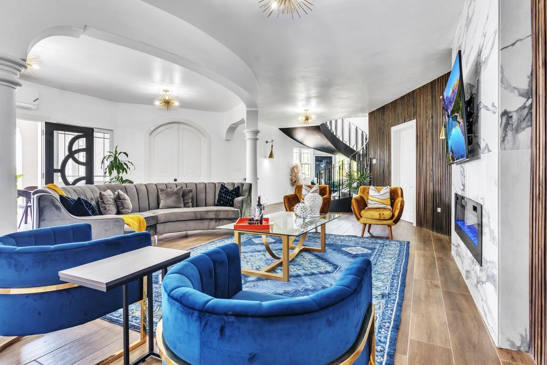 Main living room with blue velvet chairs, a curved grey sofa, and the spiral staircase beyond