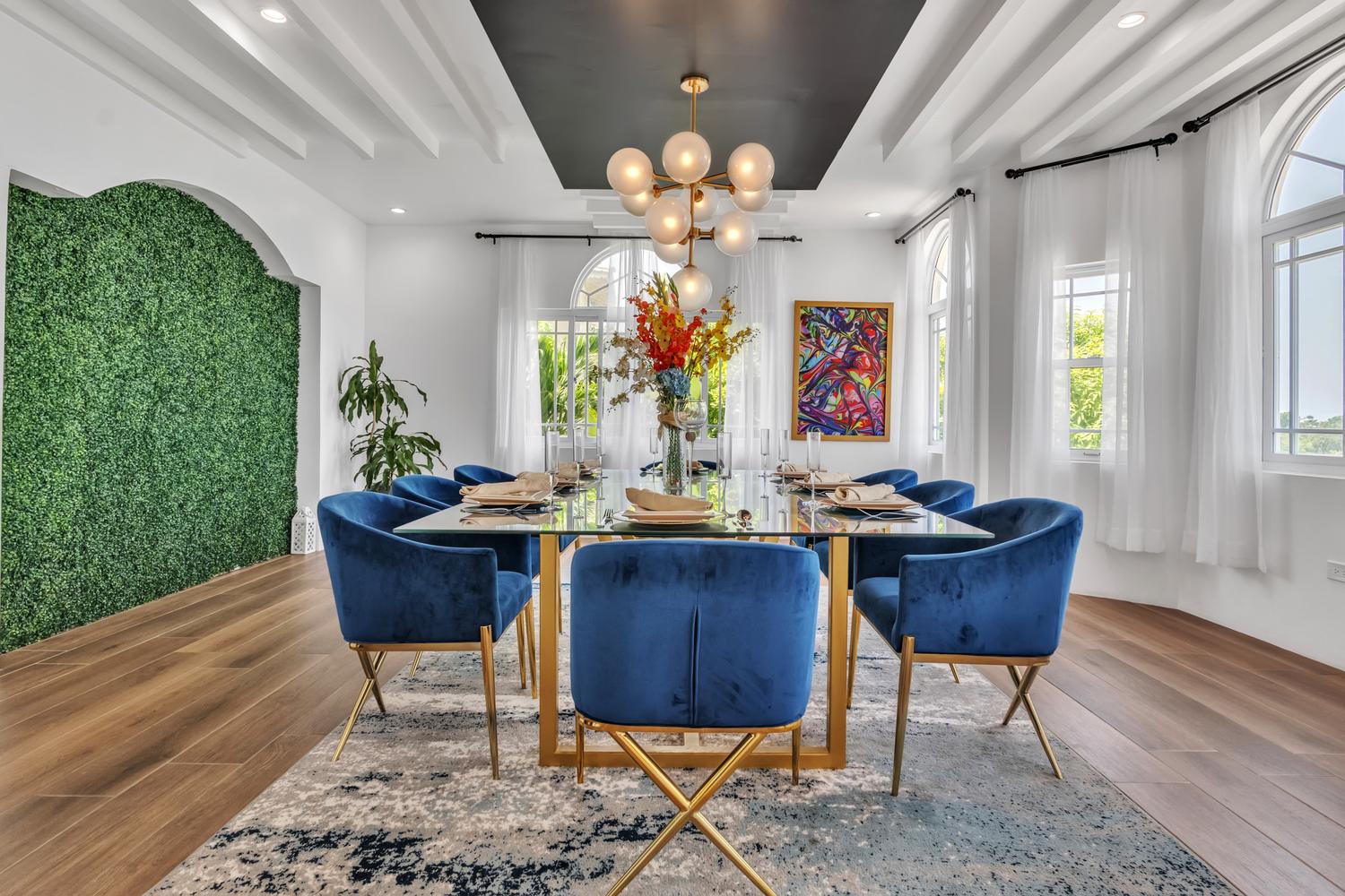 The villa dining room with blue velvet chairs, a gold and glass table, and a living green wall