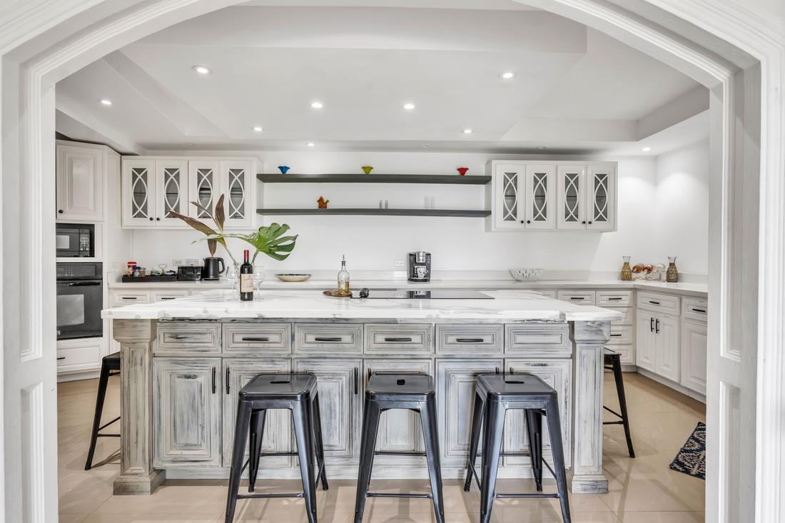 White kitchen with a large marble island and black stools