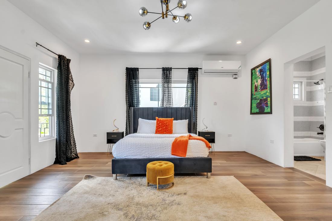 Bedroom with a charcoal upholstered bed, orange accents, and an ensuite bath