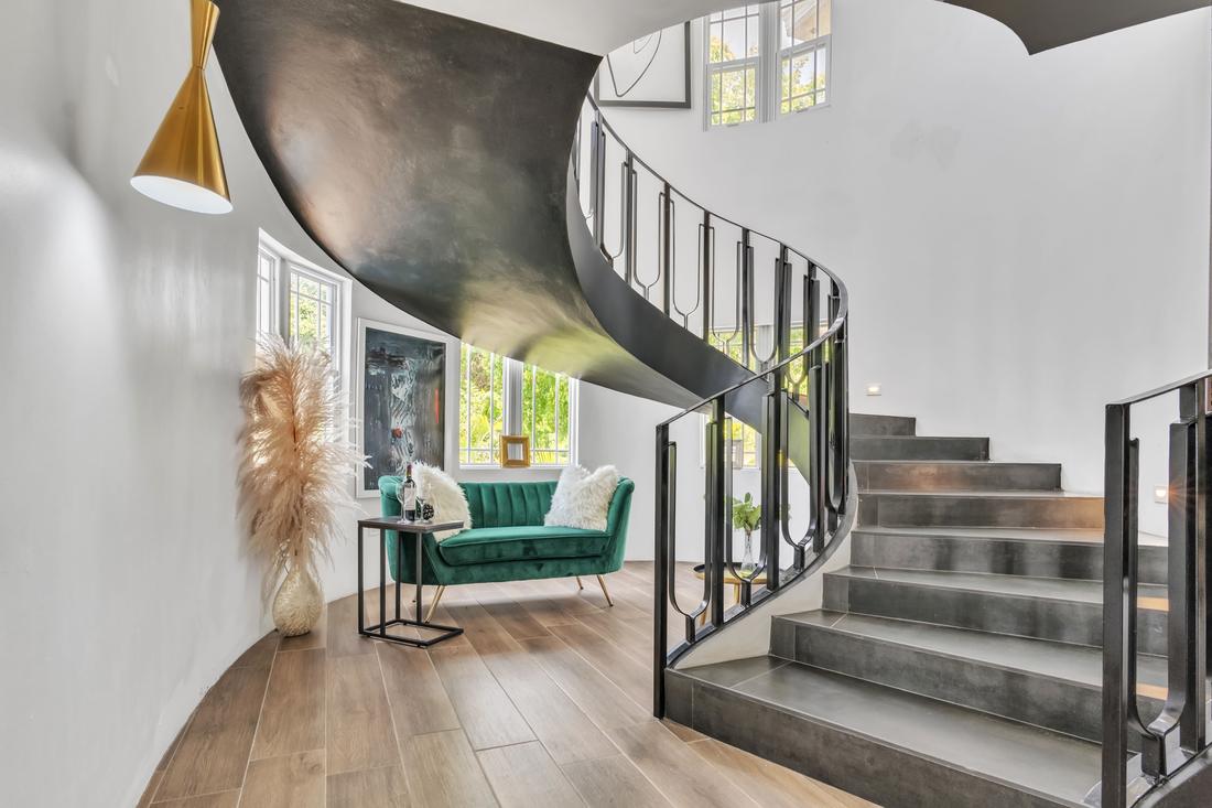 Sculptural black spiral staircase with a green velvet loveseat beneath